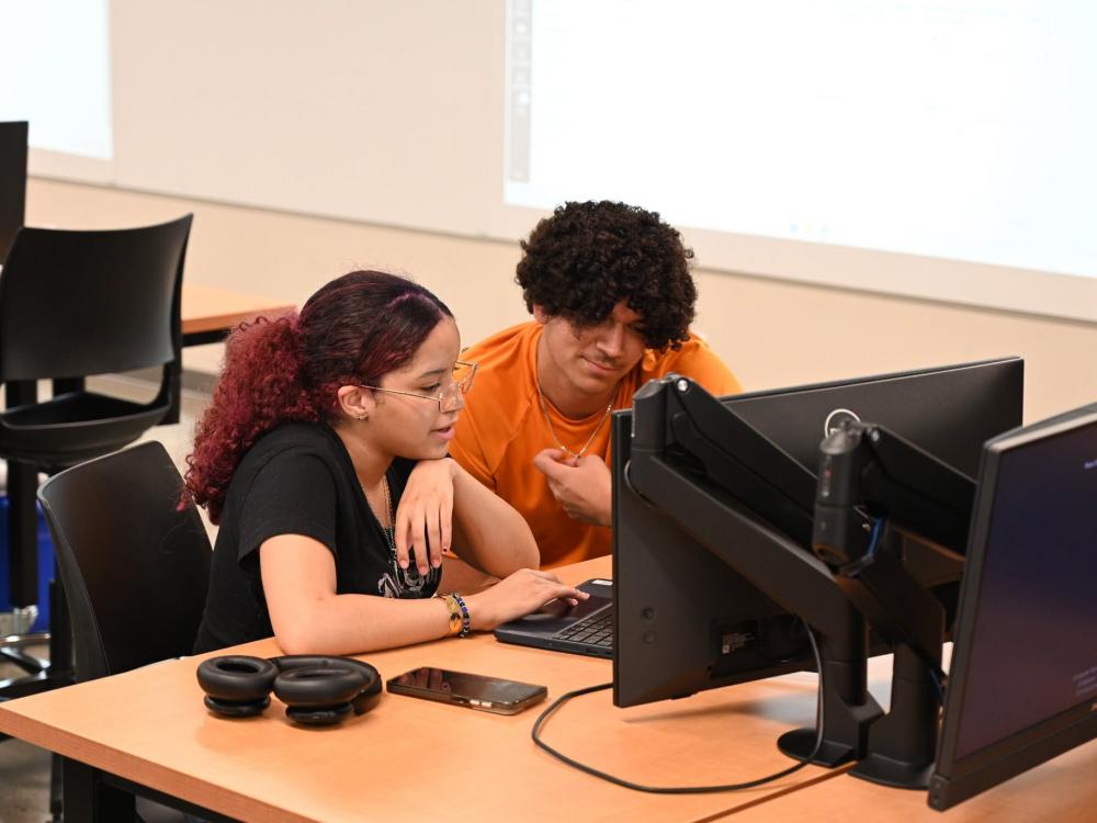Two students sitting next to each other looking at a computer