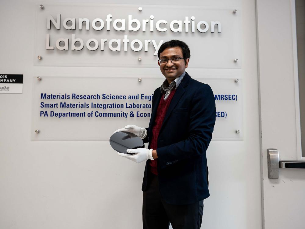 Researcher Saptarshi Das poses in front of the Nanofabrication Lab at Penn State's Materials Research Institute, smiling and holding a silicon wafer used as a foundation in circuit construction