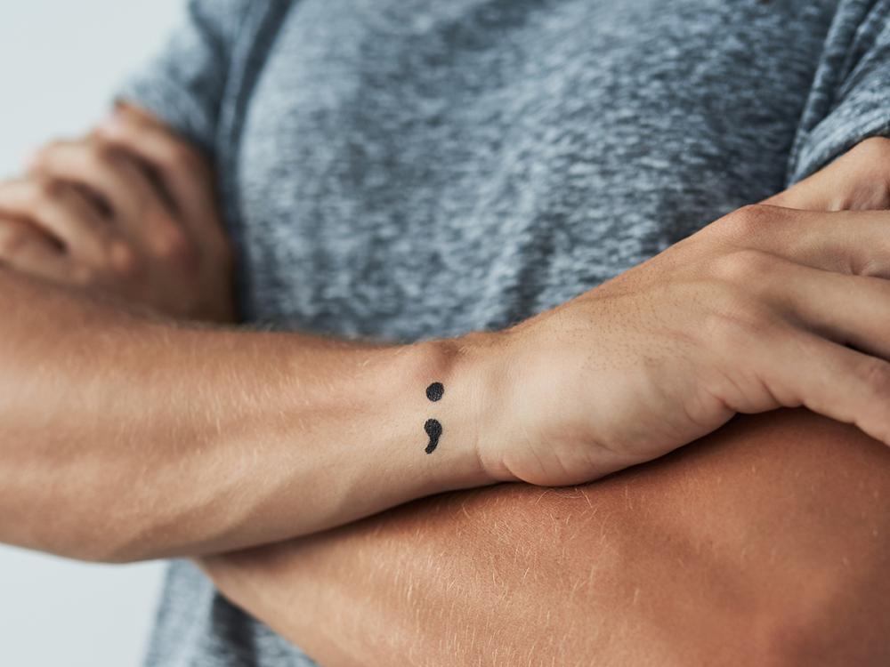 Close-up of crossed arms showing a semicolon tattoo on the wrist.