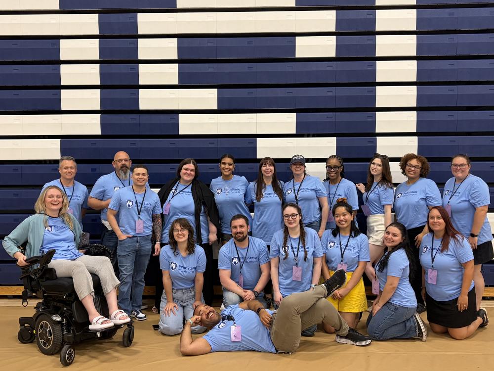 A group of people wearing matching blue T-shirts pose in front of a group of bleachers.
