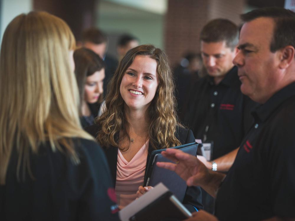Female student speaking and smiling with employers at the career fair
