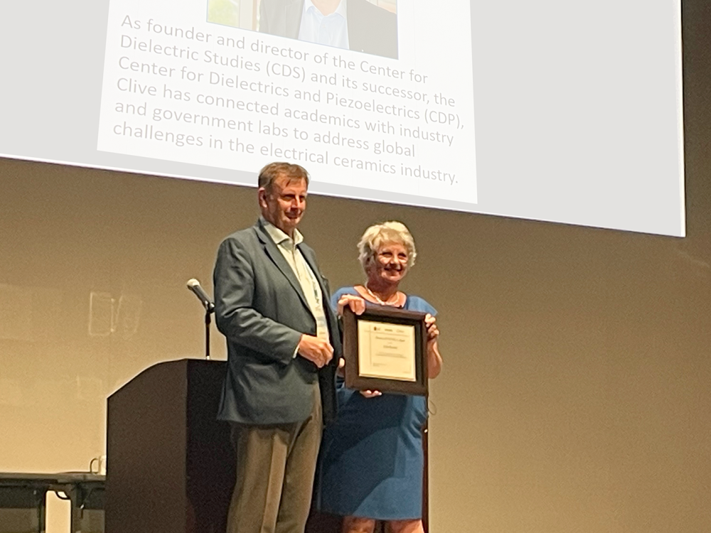 Man receiving an award from a woman on a conference stage