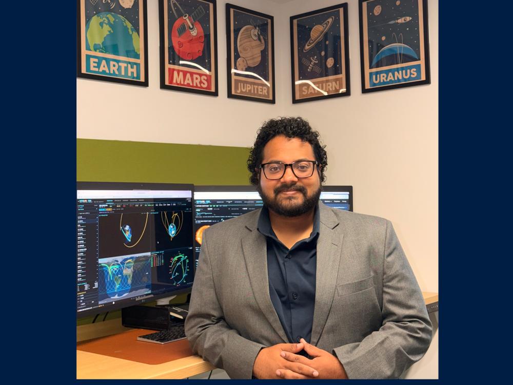An assistant professor of aerospace engineering sits in his office surrounded by a computer and research.