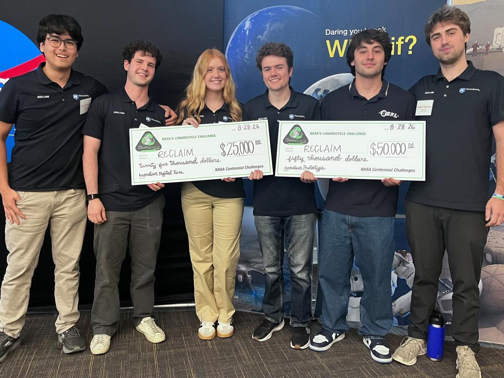 Six students from the Penn State team for the LunaRecycle Challenge pose with two large checks.