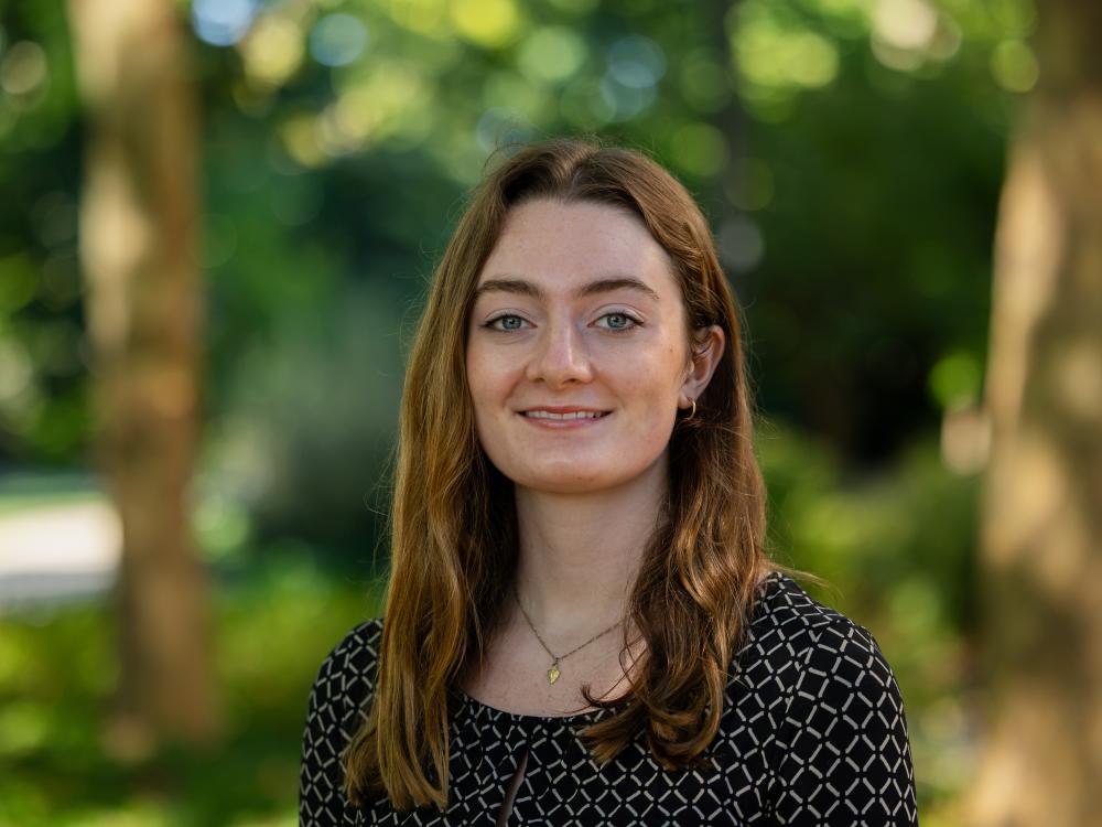 Colleen McKenzie wears a black blouse while standing outdoors in front of trees.