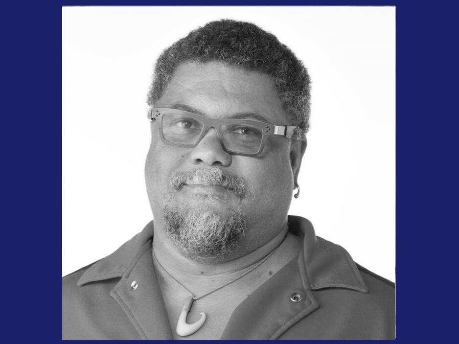 Black man with short dark hair wearing glasses and smiling