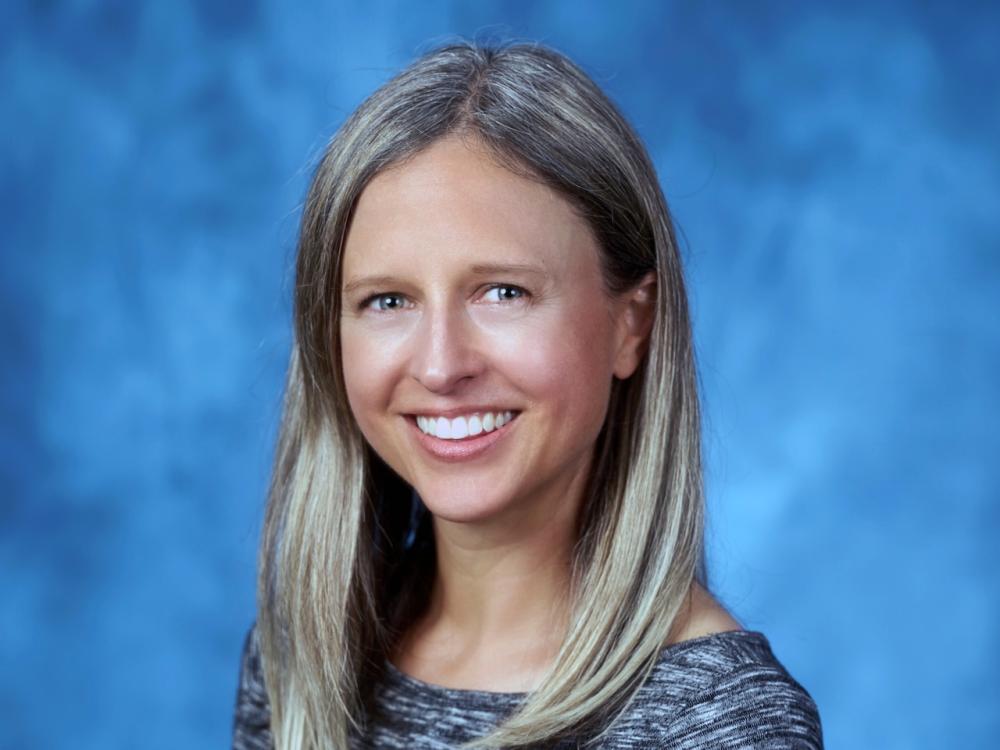 Karen Babbs Hollett smiles for a headshot against a blue background.