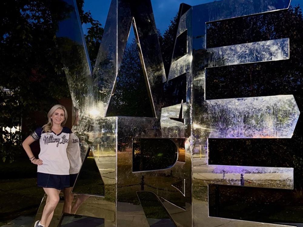 Woman stands in front of iconic We Are sign at Penn State