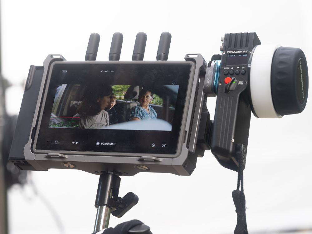 Three individuals can be seen on the viewfinder of a video camera as a commercial is being recorded