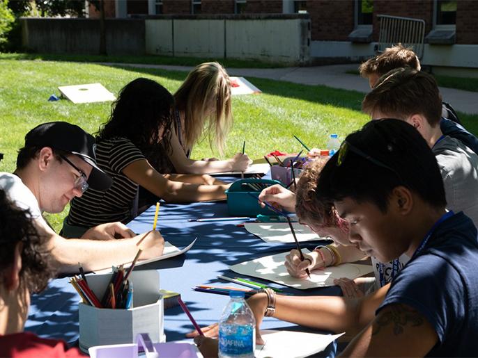 A group of college students gather around a table painting and drawing