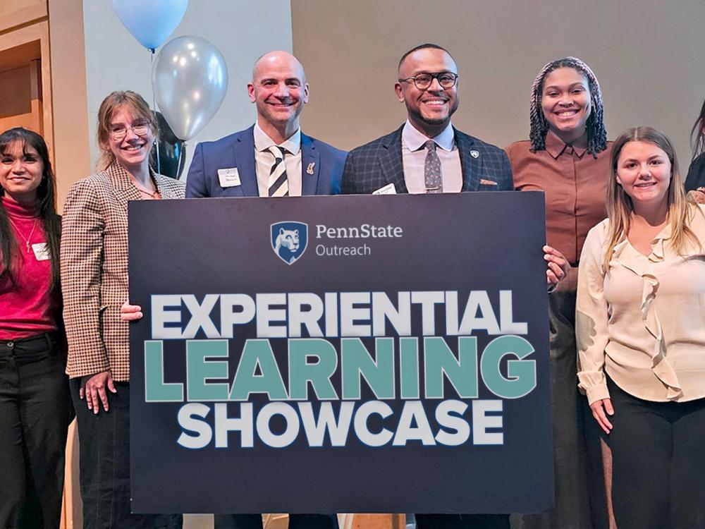 Group of smiling people holding a blue sign that reads Experiential Learning Showcase in blue and white text