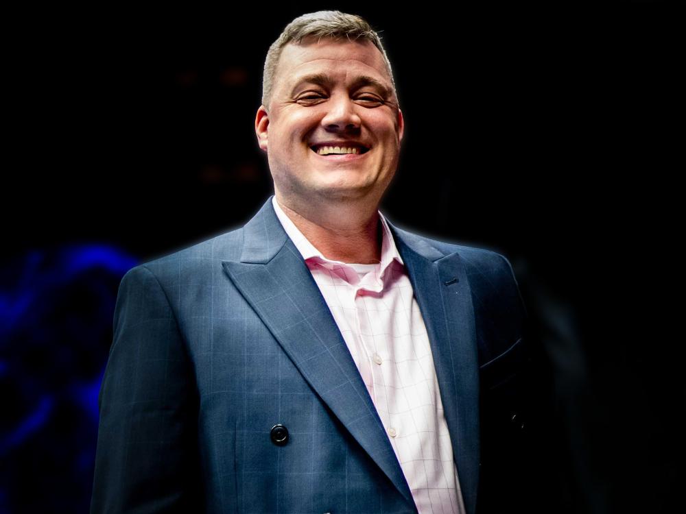 Promotional portrait of sports journalist Keith Paradise wearing a blue blazer and light-colored shirt against a dark background.