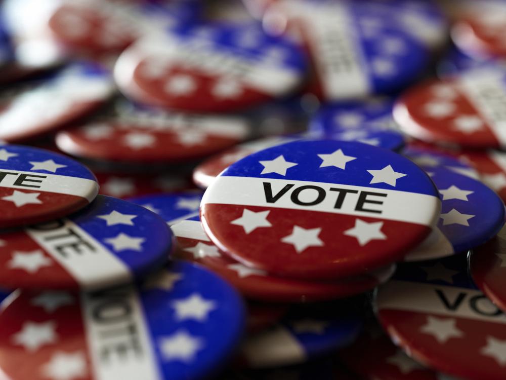 A pile of pins in red, white and blue with six white stars and a white stripe that reads "VOTE"