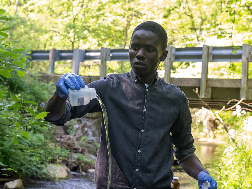 Person stands in a stream, pouring out a sample of water.