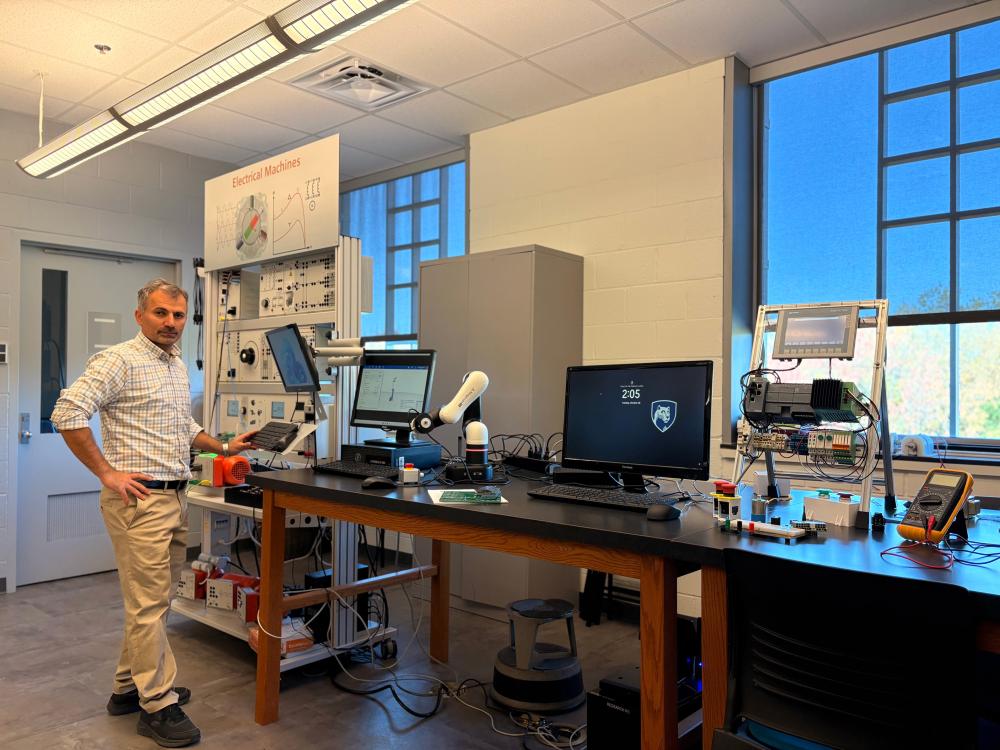 Rasoul Milasi stands in front of modern Electro-Mechanical Engineering Technology equipment.