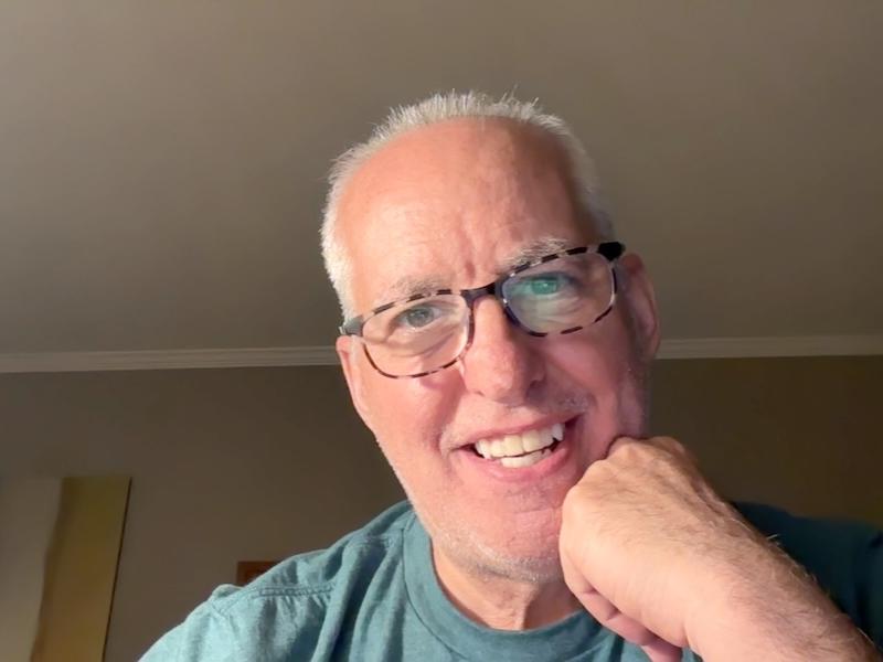 Keith Aronson headshot with short white hair, steel frame glasses, green t-shirt, smiling.