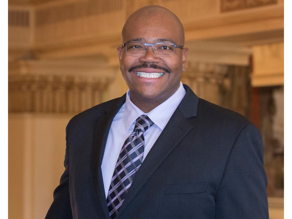 A smiling Lance Kennedy-Phillips wearing a business suit and tie