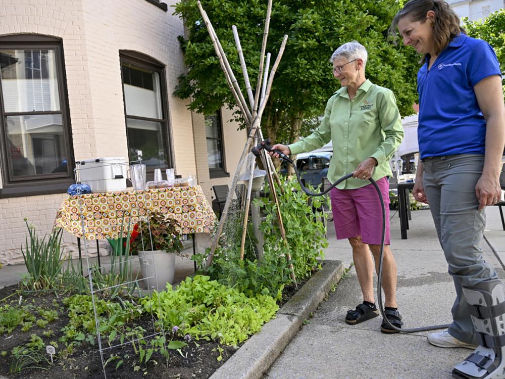 Laurie Funk, left, director of the Chestnut Street Community Center in Lebanon, holds a hose and waters a garden filled with lettuce and other produce. Laurie Crawford, Penn State Health program manager for food access, stands next to her.