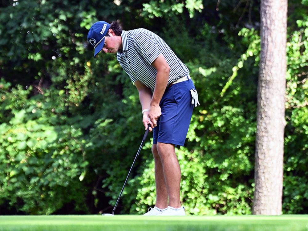 Max Mottura prepares to putt on a golf course, wearing a Penn State cap and striped shirt.