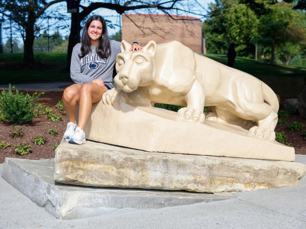 Natalie DiMario sitting next to the Nittany Lion shrine on top of the concrete slab it sits on