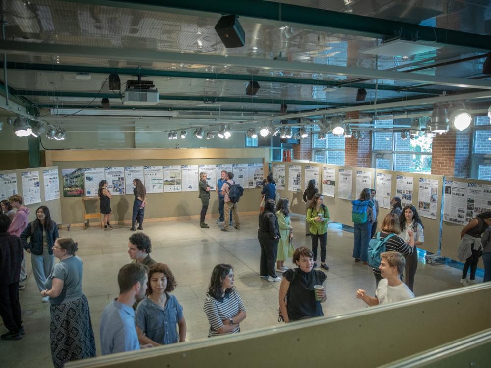People gather in a bright indoor gallery to view research posters displayed along the walls and talk with one another.
