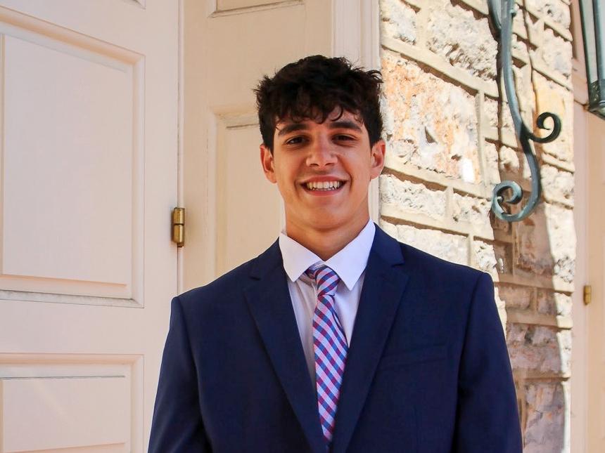 Nikolas Papoutsis, wearing a black suit and colorful tie, smiles in front of Old Main.