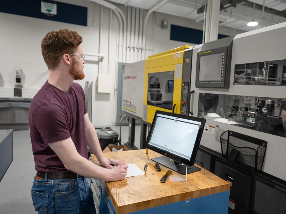 A student stands at a monitor in a lab
