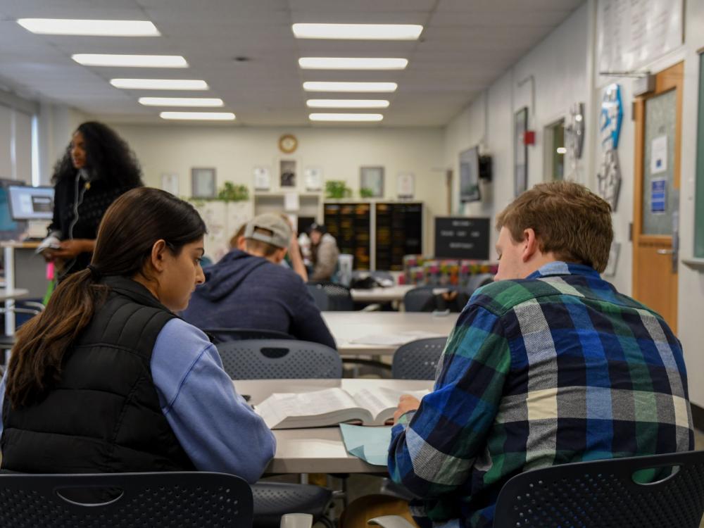 Two people sitting at desk examining textbook