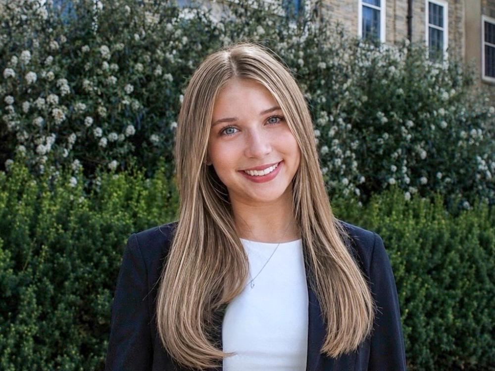 Alexa Pippy, a young woman with long blonde hair wearing a black blazer and white top, smiles outside Penn State’s Old Main building.