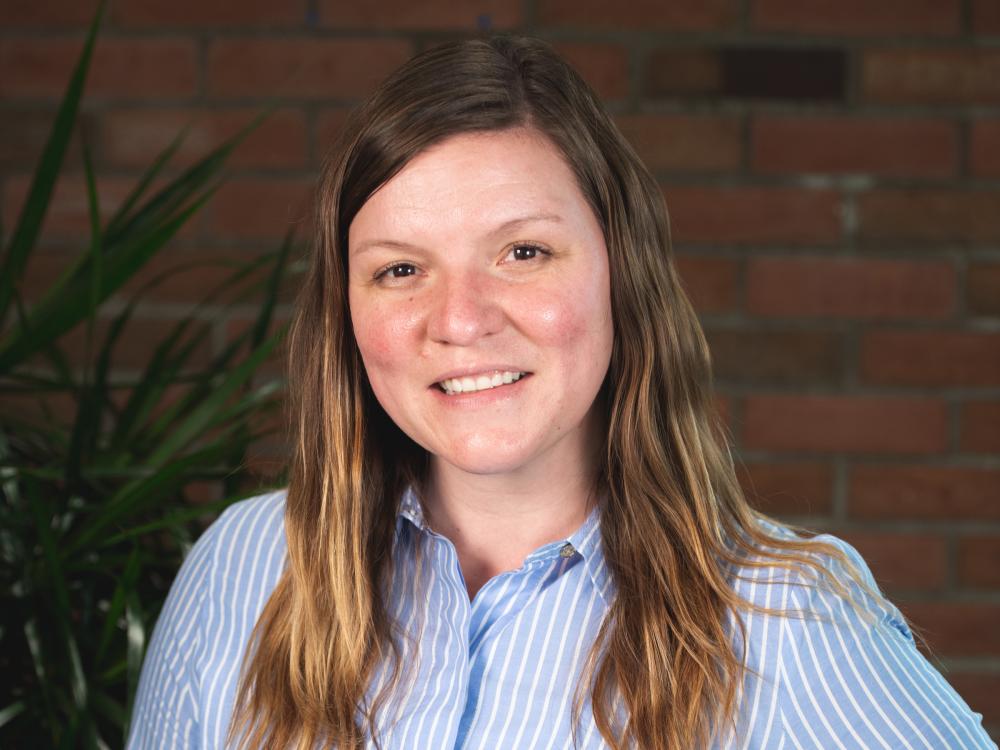 Portrait of woman with long dark hair wearing a blue button up shirt with white stripes