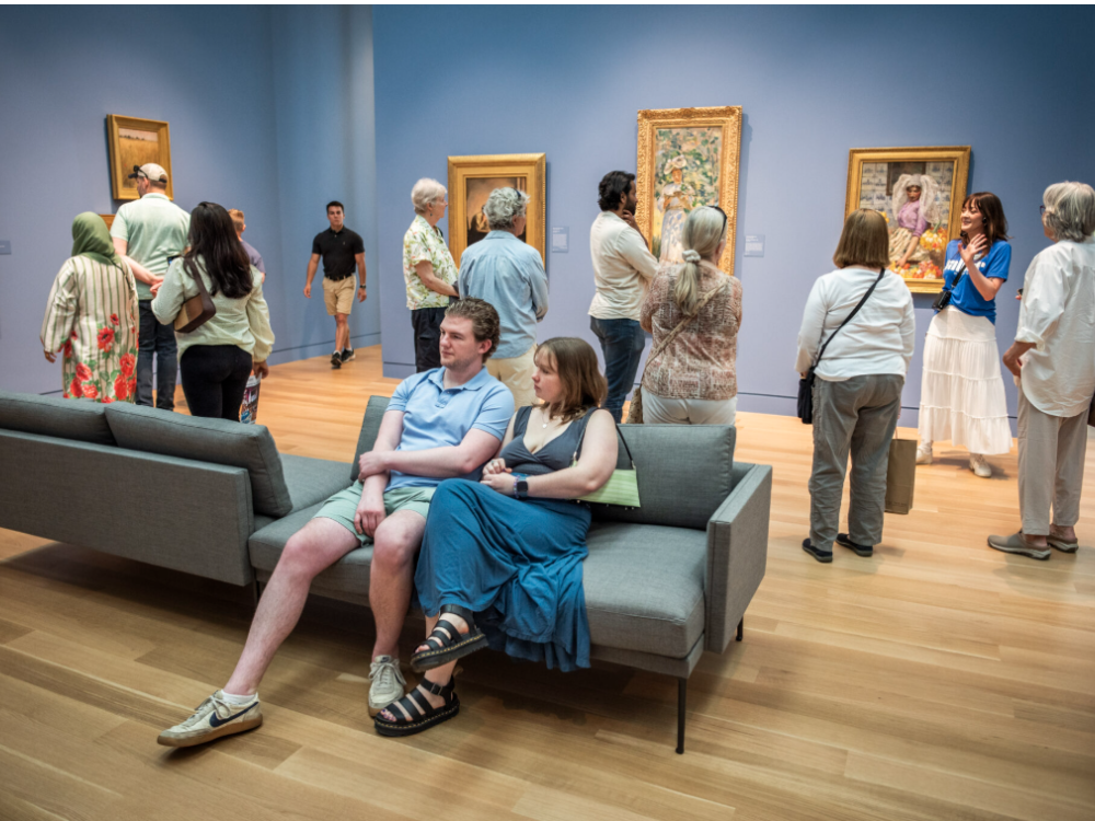People sitting and walking through a museum with paintings on the blue walls