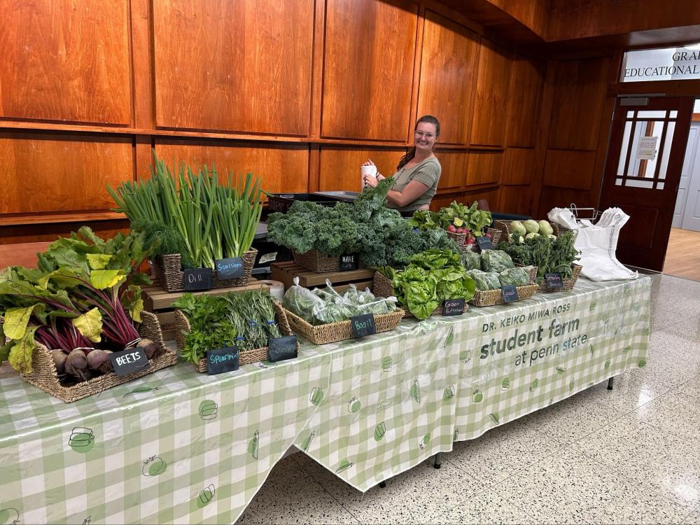 A farm staff member smiles behind a table of produce.