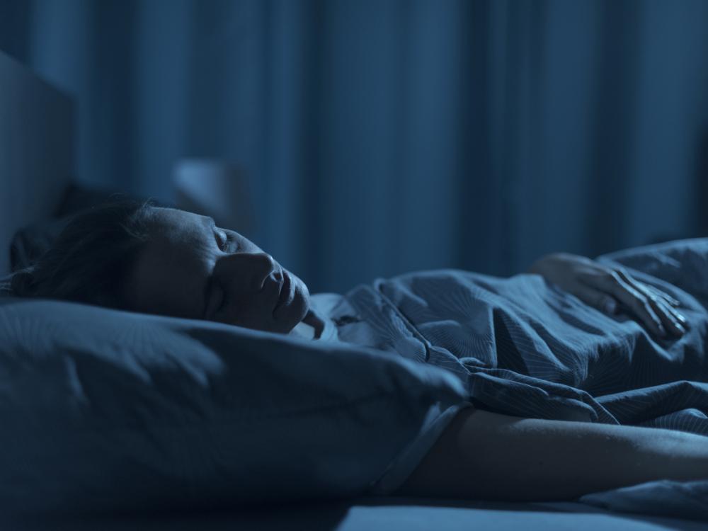 Young woman sleeps peacefully on her back in a bed in a dark room.