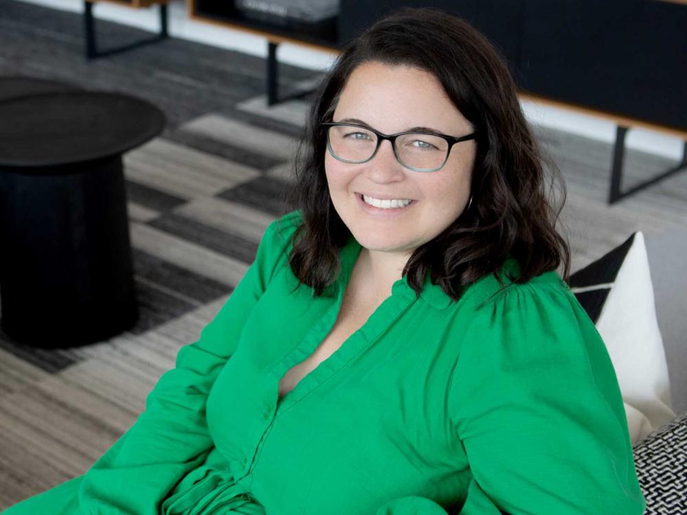 A photo of a smiling Liz Minne, who smiling while sitting and wearing glasses
