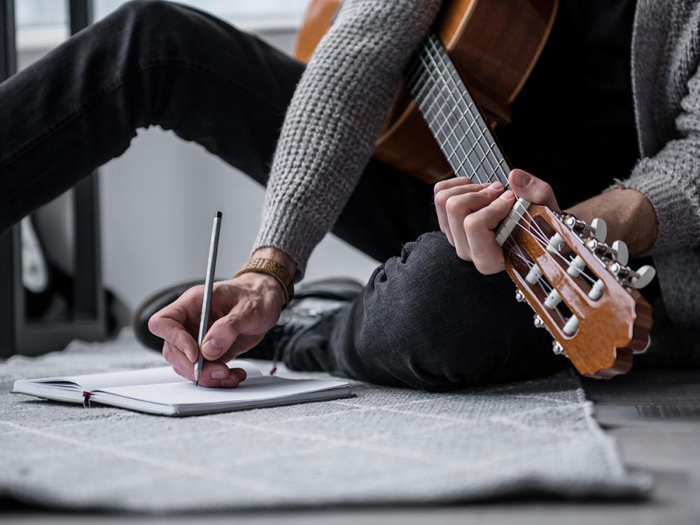 Person writes in a notebook while holding an acoustic guitar.