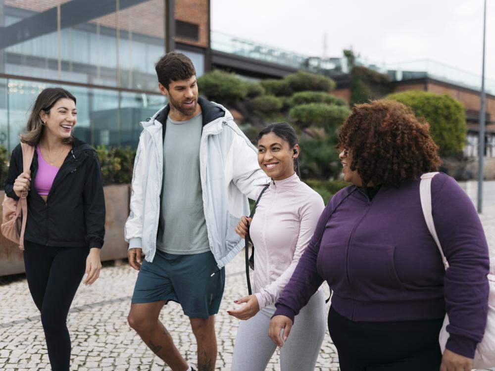 Four happy students in active wear walk across a college campus