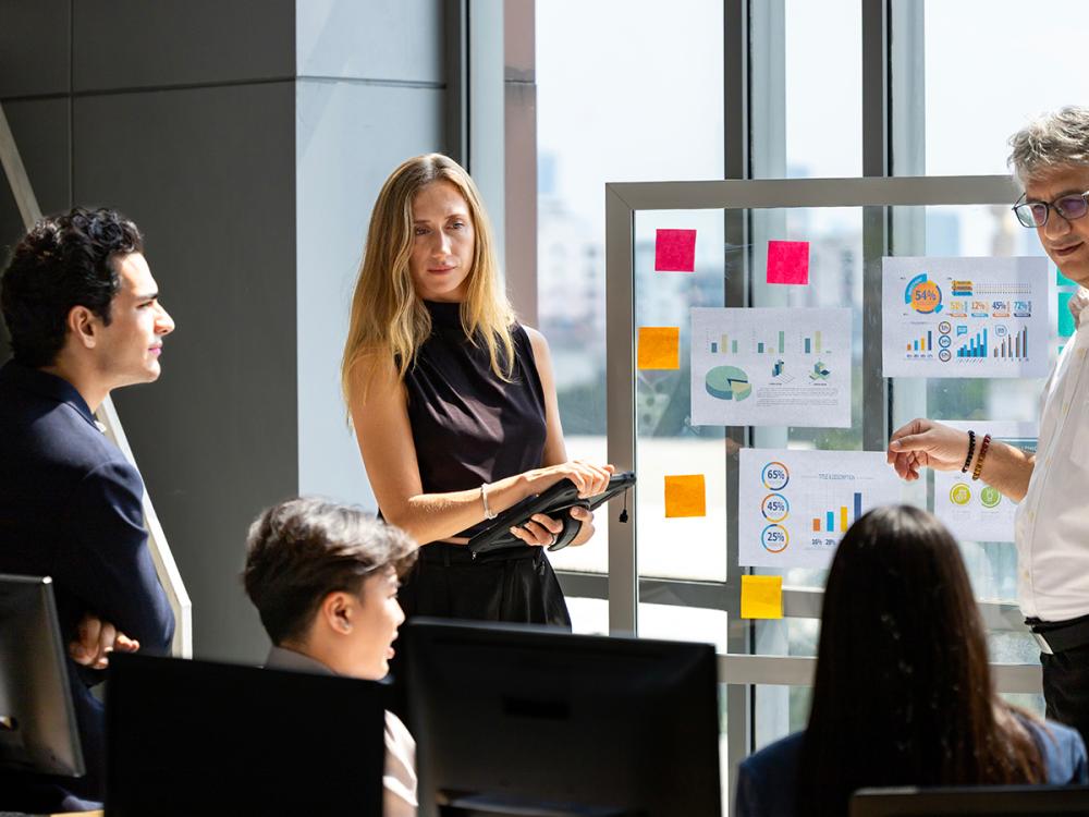 Business team reviews charts and graphs on a presentation board in a bright office.