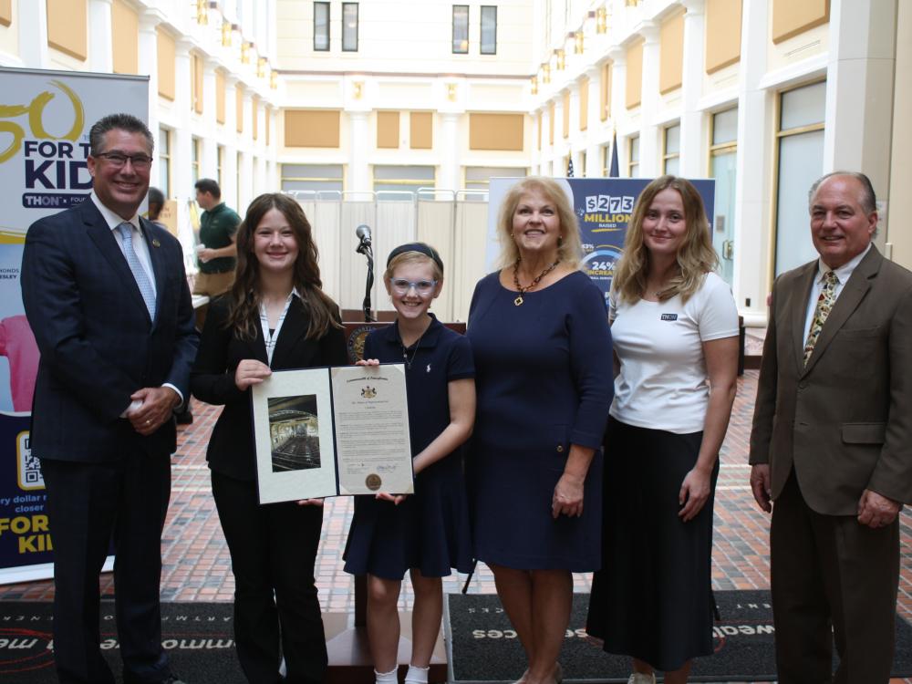 Six people pose with a ceremonial document at a THON and Four Diamonds event.