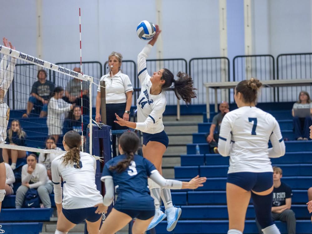 A member of the Penn State Behrend women's volleyball team spikes the ball at the net.