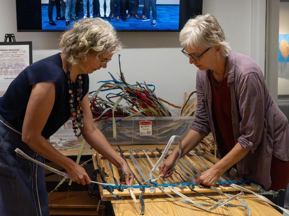 two women weaving cloth on a table