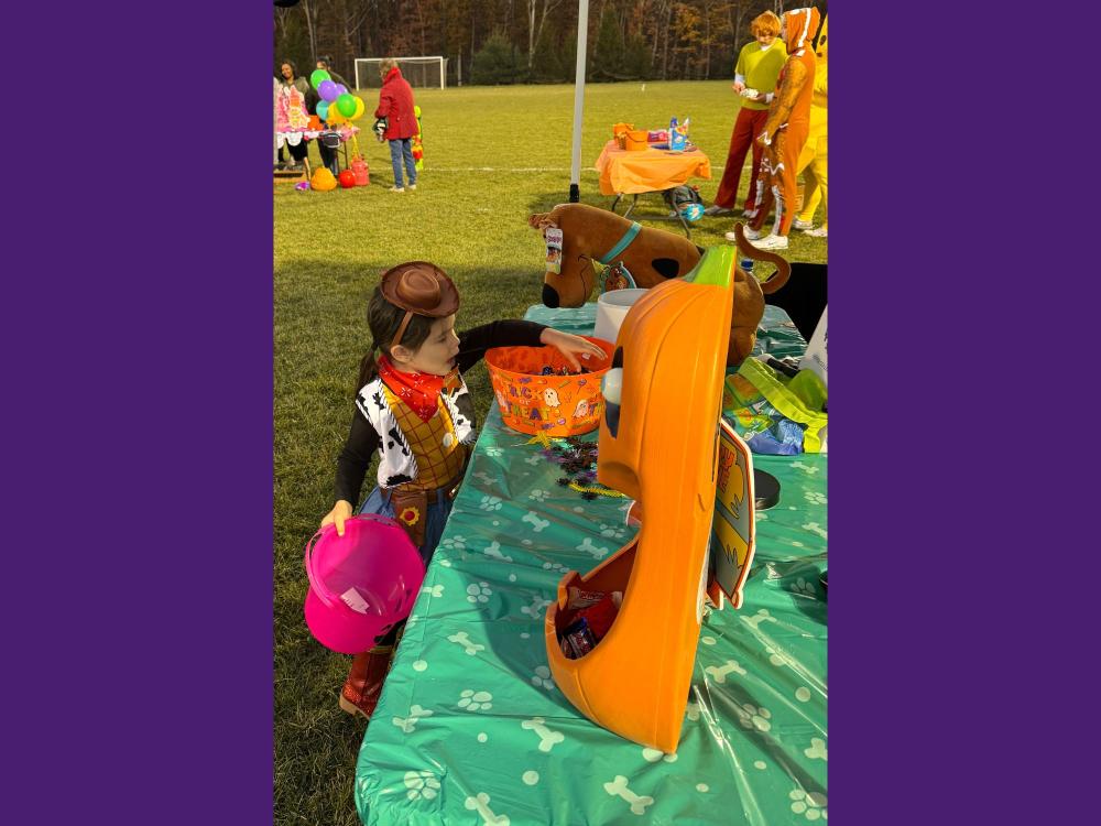 A young girl in a cowgirl costume picks candy from a bowl.