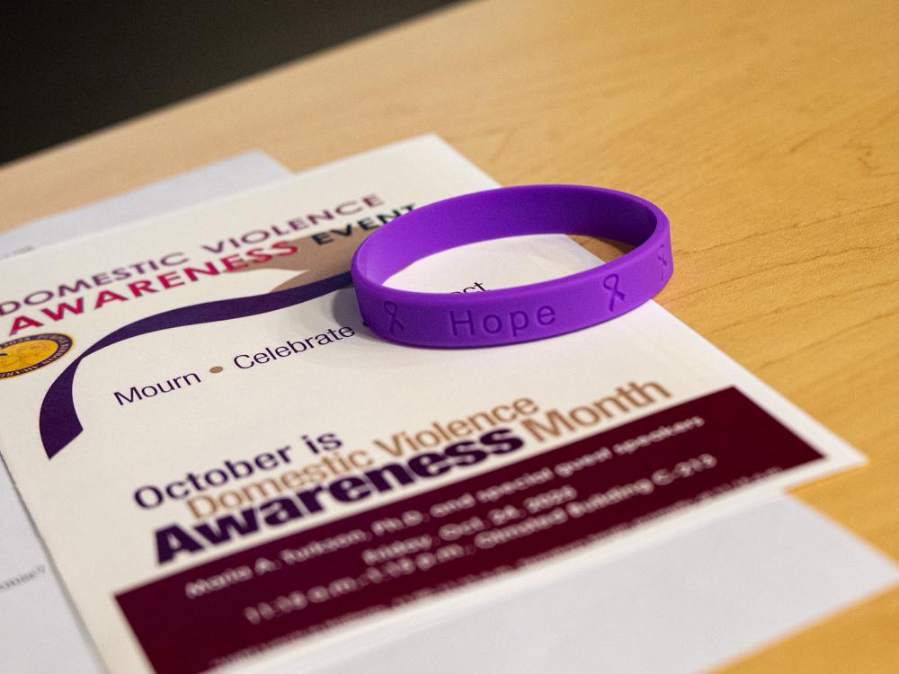 A purple bracelet with the word "hope" and a program for a Domestic Violence Awareness event lay on a table