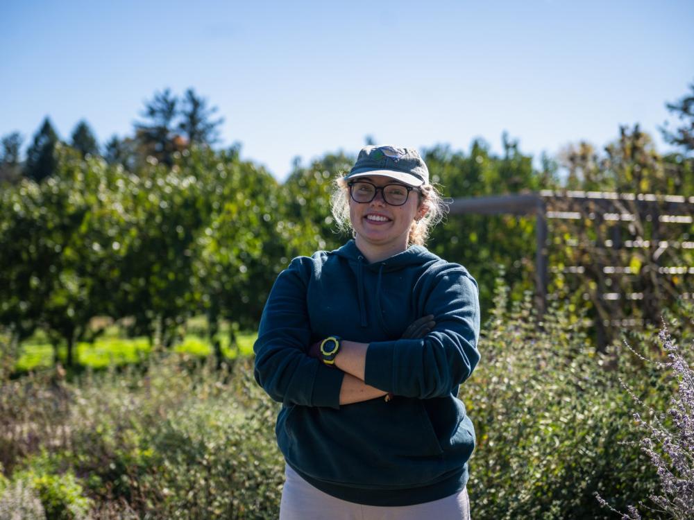A student wearing a hat poses for the camera in an outdoor setting