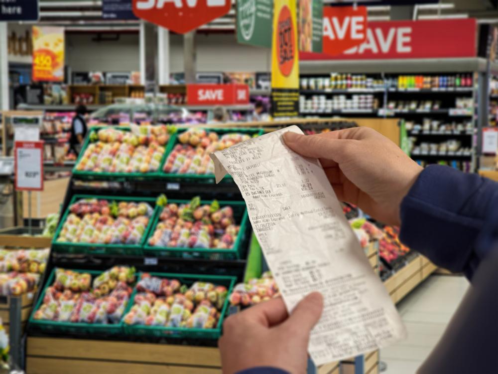 A pair of hands holds up a receipt in a grocery store