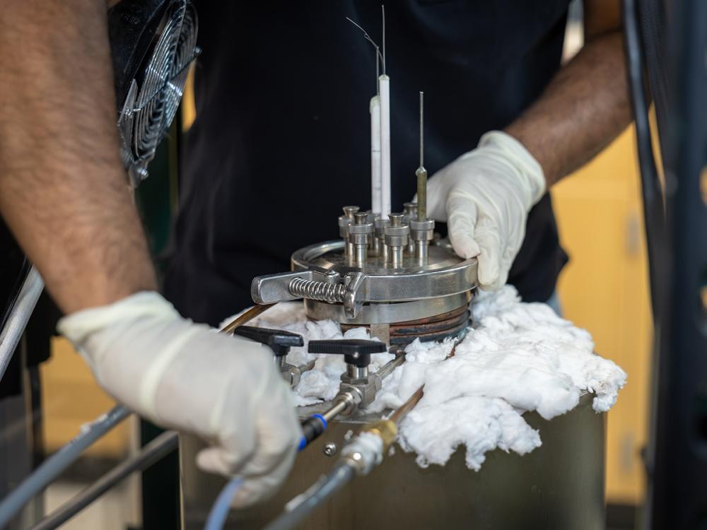 A person wearing gloves closes the lid of a small reaction chamber in a lab.