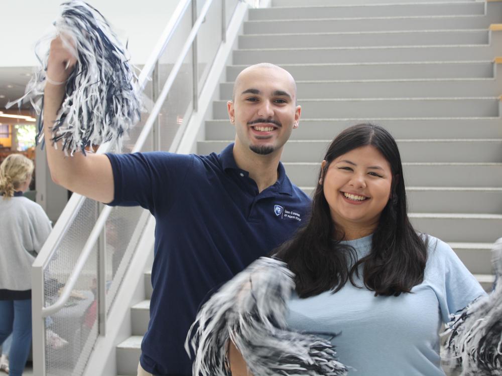 Two students holding blue and white pom poms at an event at Penn State University Park campus