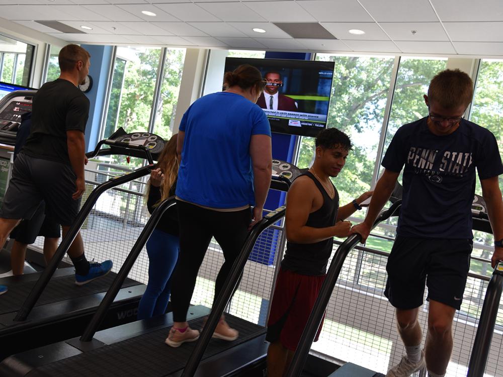 People exercise on treadmills in a bright fitness center with large windows.