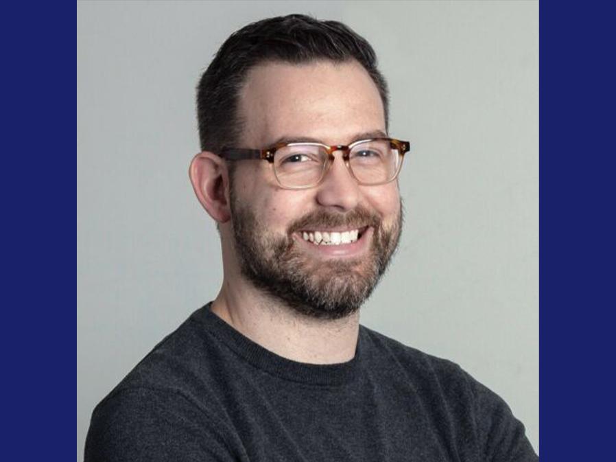Portrait of a smiling person with brown hair and glasses