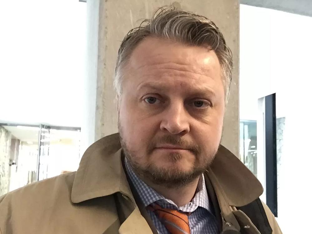 Man with salt and pepper hair wearing a brown trench coat