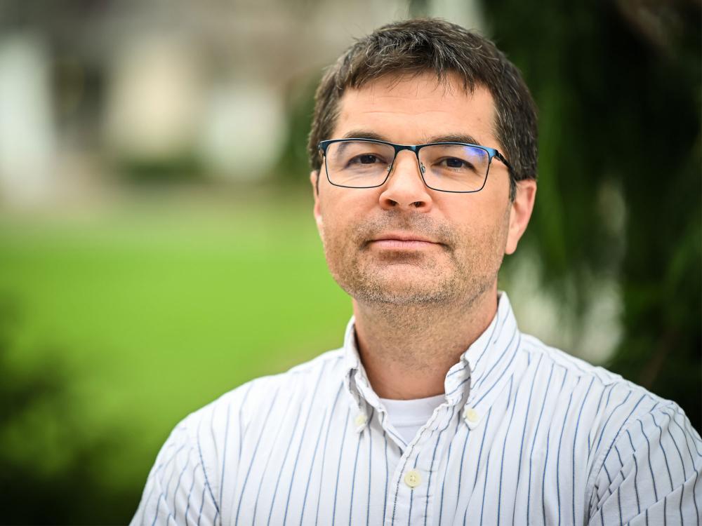 A photo of lead researcher Nathaniel Warner looking sternly at the camera in front of greenery